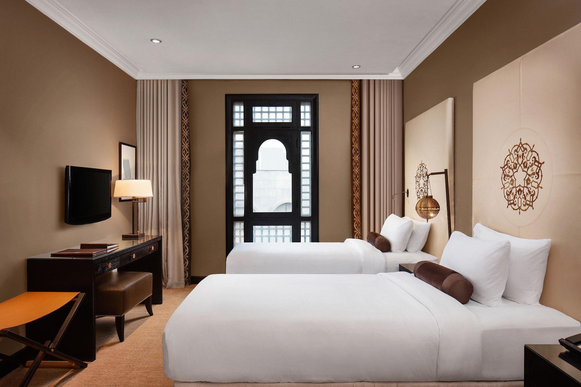 Sofitel Shahd Al Madinah Hotel Medina Buitenkant foto The photo shows a well-decorated hotel room featuring two single beds with white bedding. The walls are a warm beige color, and there are decorative elements such as patterned wall panels and a large window with an elegant design. In the room, there 